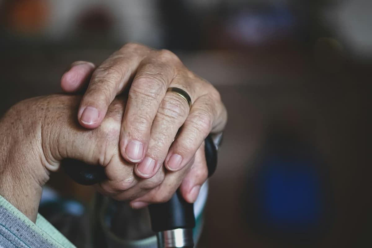 Close-up of wrinkled hands resting on a walking cane